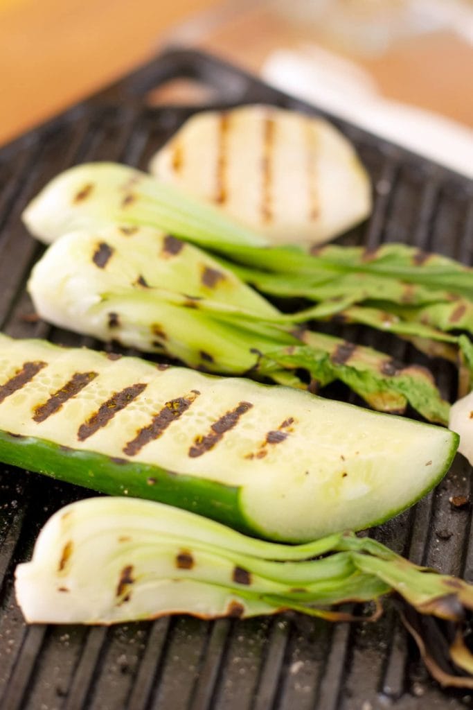 shallow depth of field close up of vegetables being grilled. boy choy, cucumber and kohlrabi all have clear defined grill marks on its surfaces.