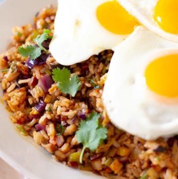 Vegetarian kimchi fried rice topped with 3 fried eggs and served on a round white plate.