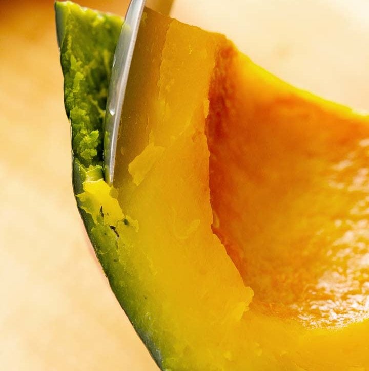 closeup of separating the peel from the flesh of a piece of cooked kabocha squash with a metal spoon