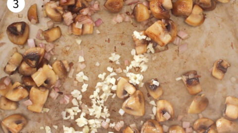 Browned diced mushrooms in a pan with minced garlic added.