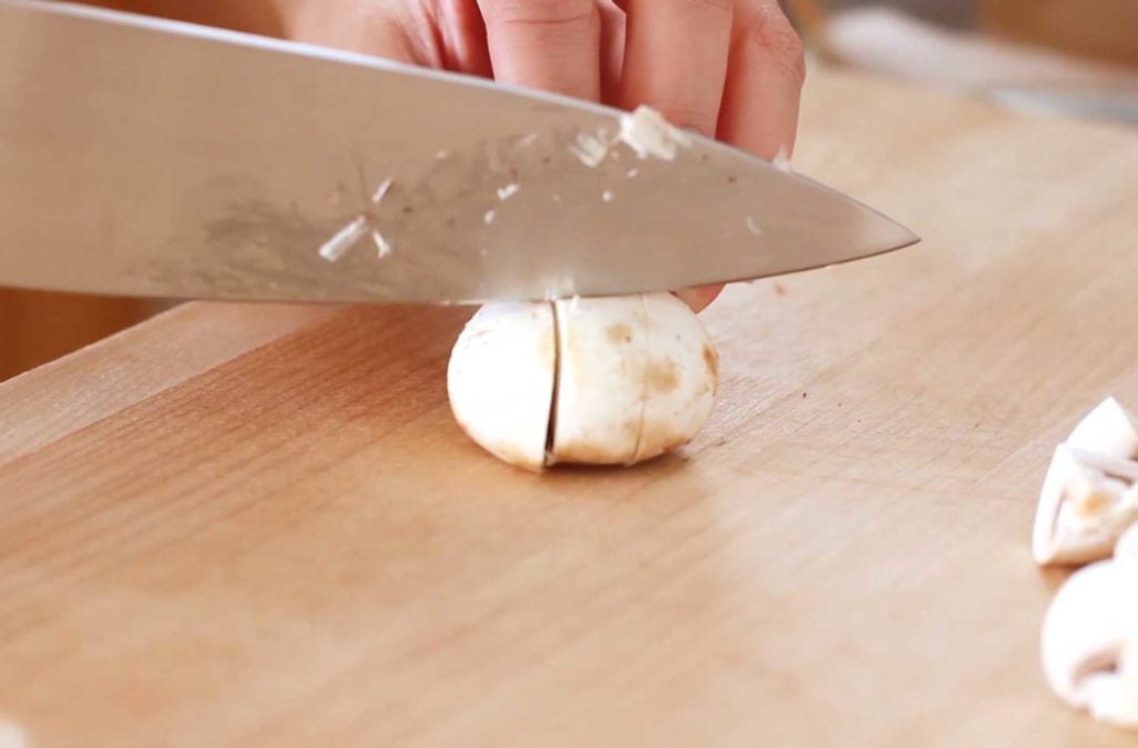 Sliced white button mushroom on a wood cutting board.