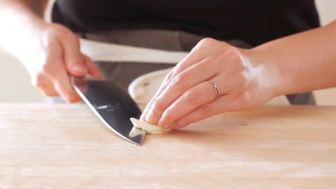 A person making horizontal slices on a smashed garlic clove.