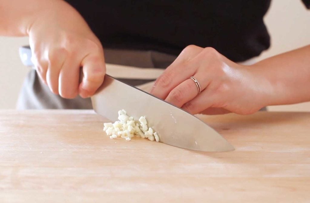 A person mincing garlic on a wood cutting board.