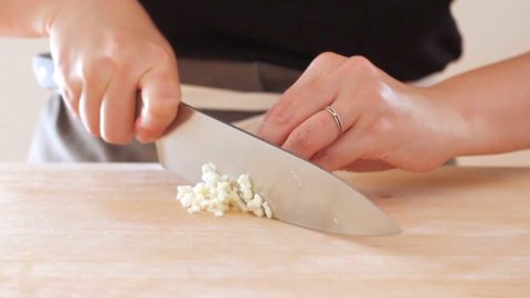 A person mincing garlic on a wood cutting board.