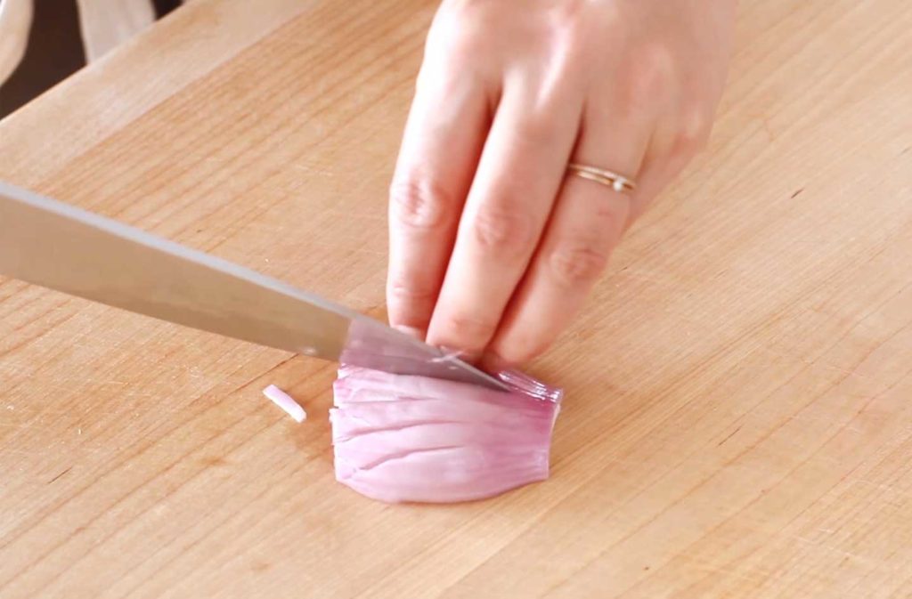 A shallot being sliced on a wood cutting board.