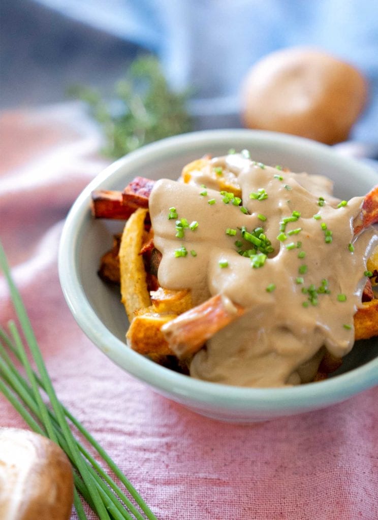 Vegetable fries in a light blue bowl covered with vegan mushroom gravy and fresh chopped chives.