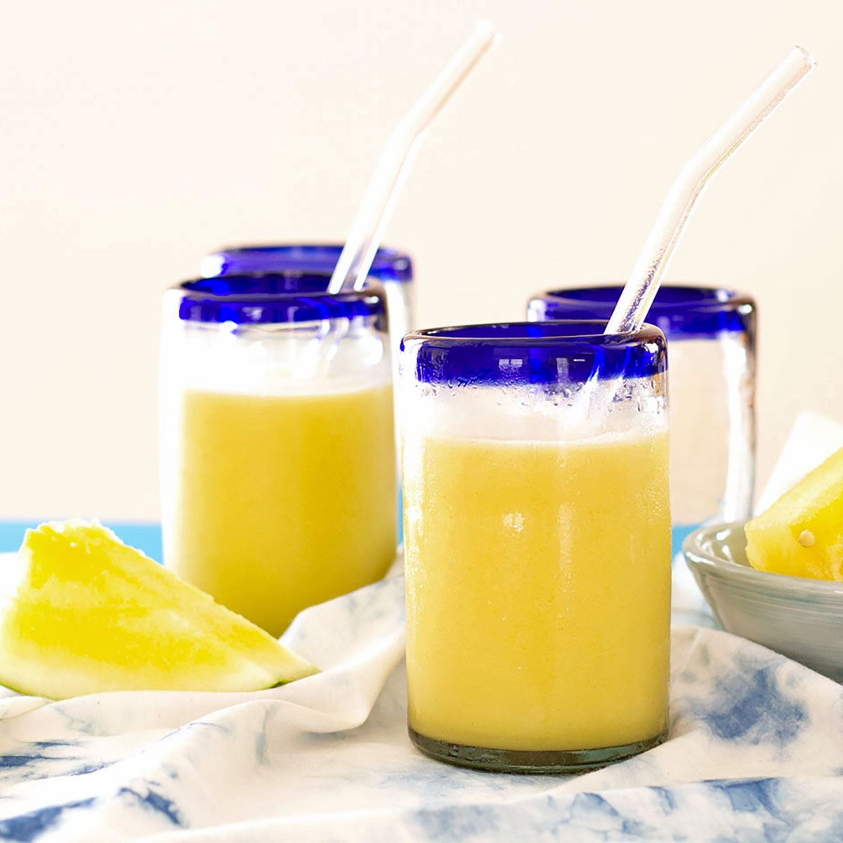 Two blue rimmed glasses filled with yellow coconut watermelon milk.