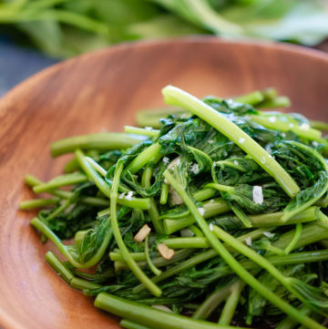 A close up view of the cooked water spinach on a wood plate.