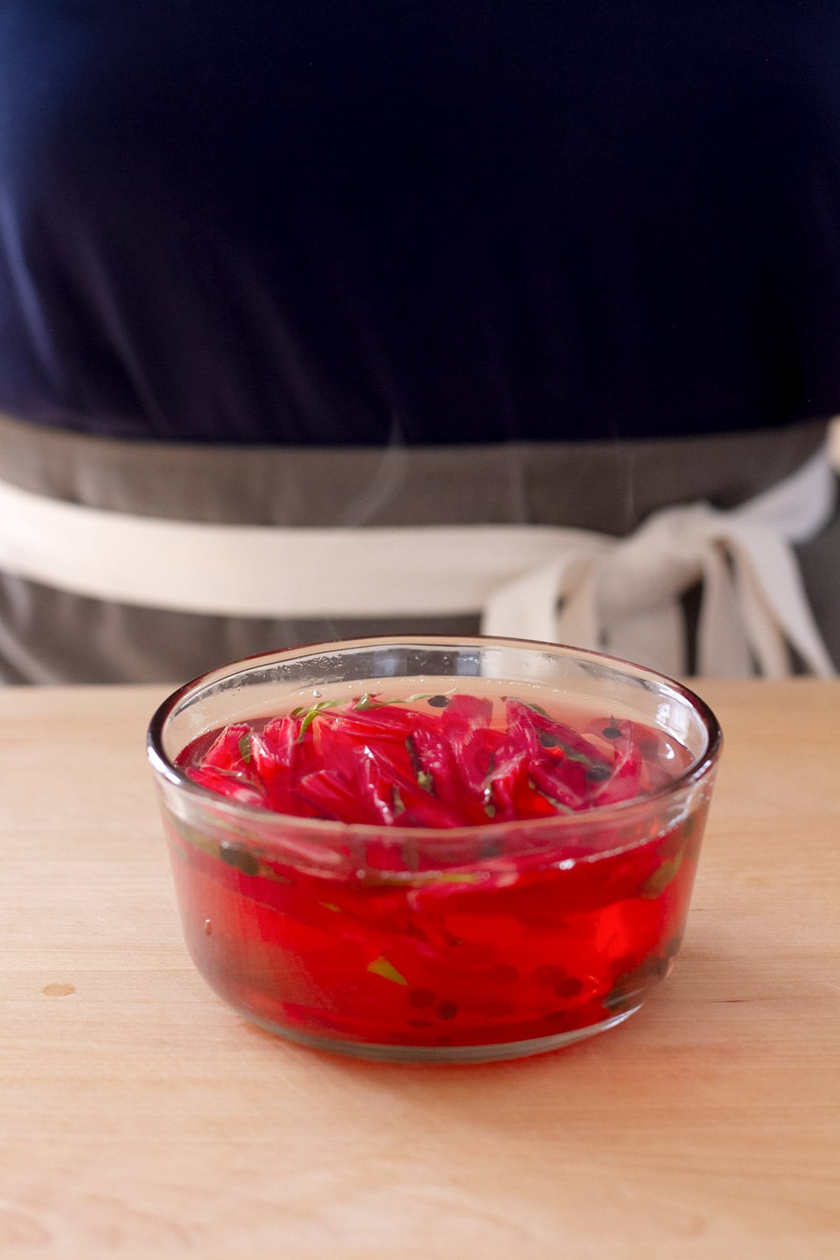 Quick pickled red swiss chard stems in a small glass pyrex container submerged in steaming hot pickling liquid.