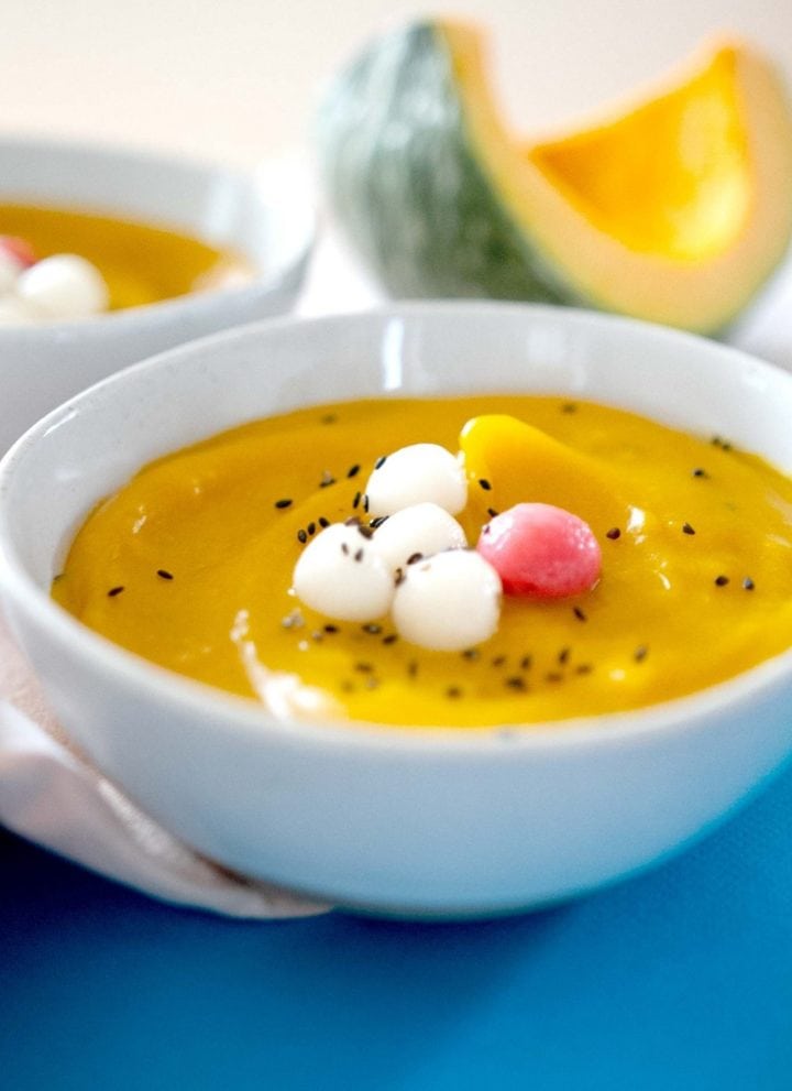 A bowl of Korean kabocha squash porridge with white and pink sweet rice balls on a blue surface.
