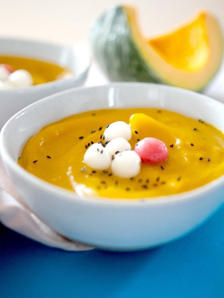A bowl of Korean kabocha squash porridge with white and pink sweet rice balls on a blue surface.