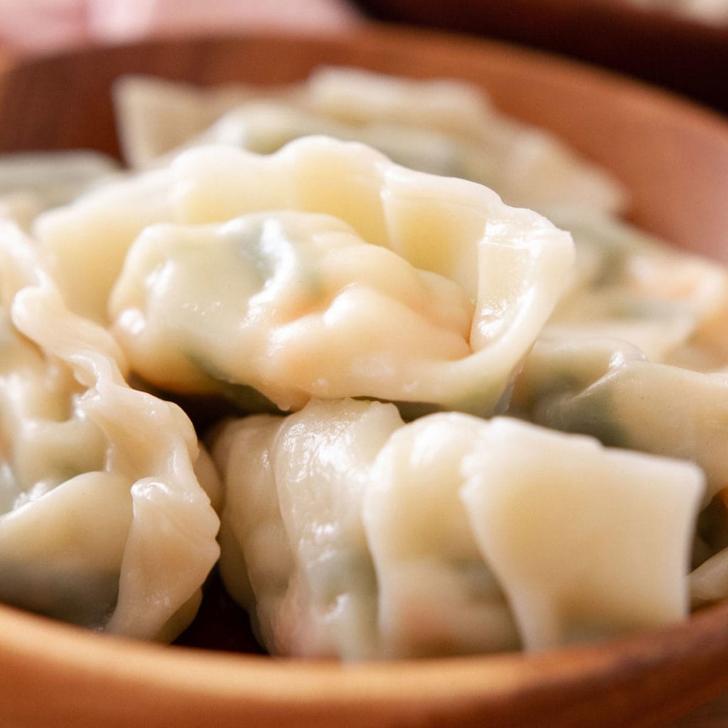 Boiled dumplings filled with snow pea leaves and shrimp in a wood bowl.