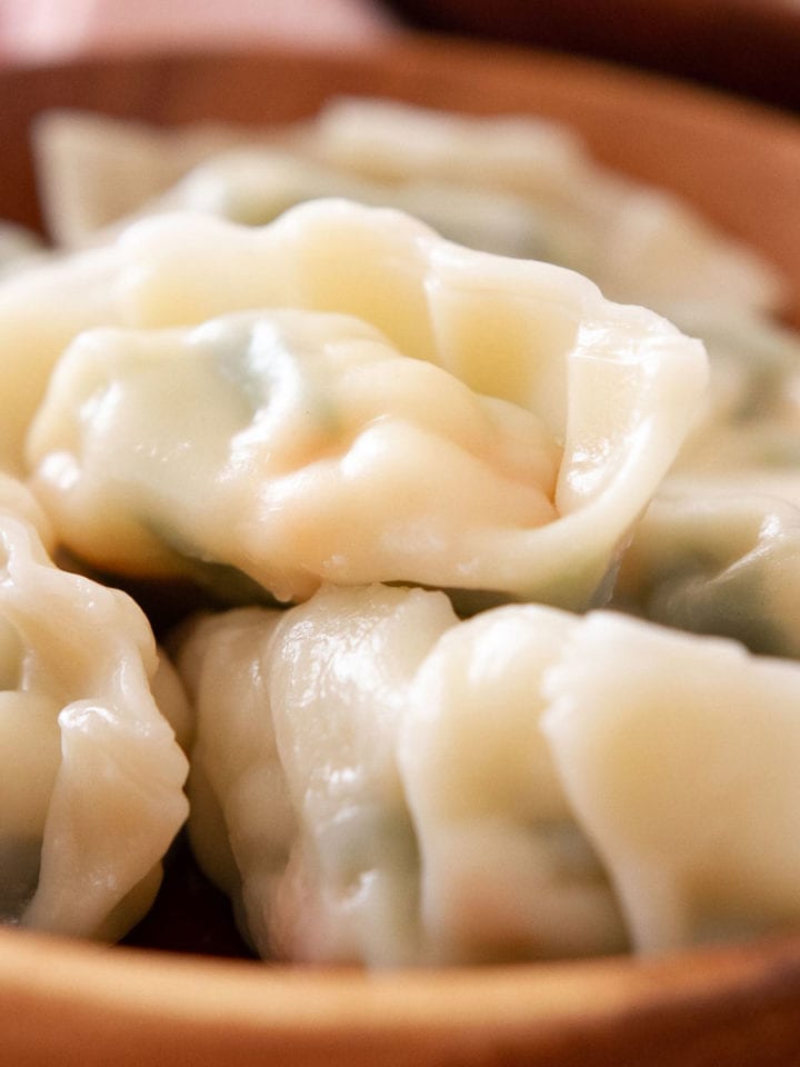 Boiled dumplings filled with snow pea leaves and shrimp in a wood bowl.