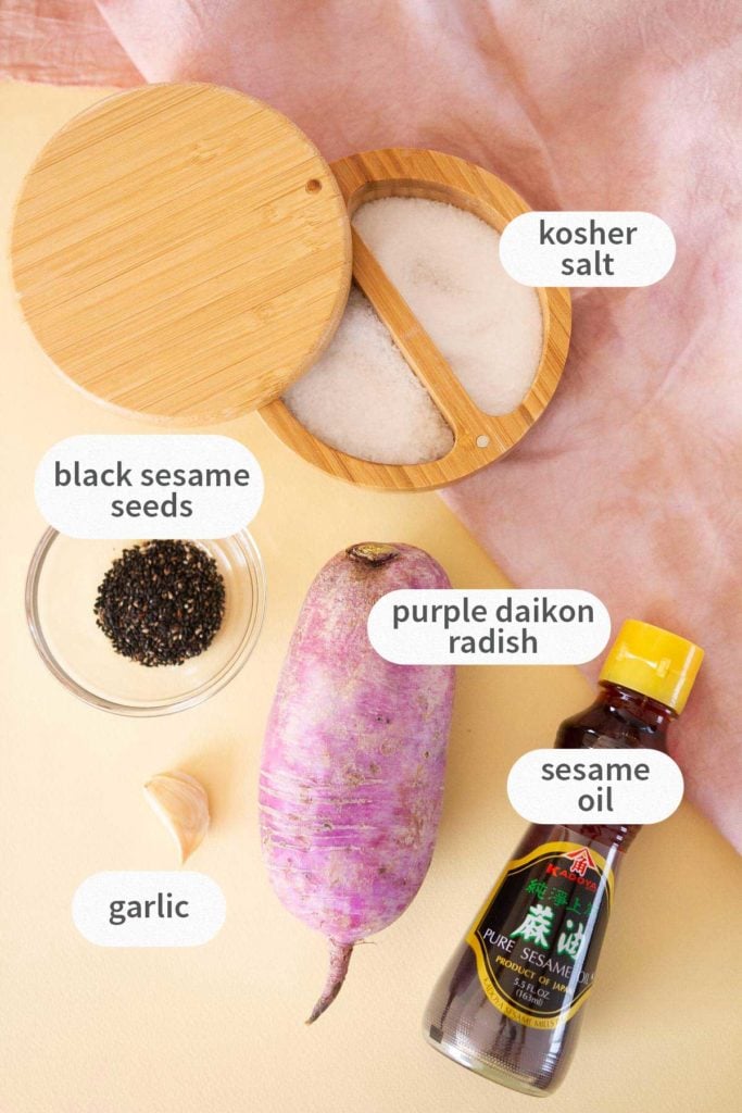 Top down view of labeled ingredients for this recipe: kosher salt, black sesame seeds, purple daikon radish, garlic, and sesame oil