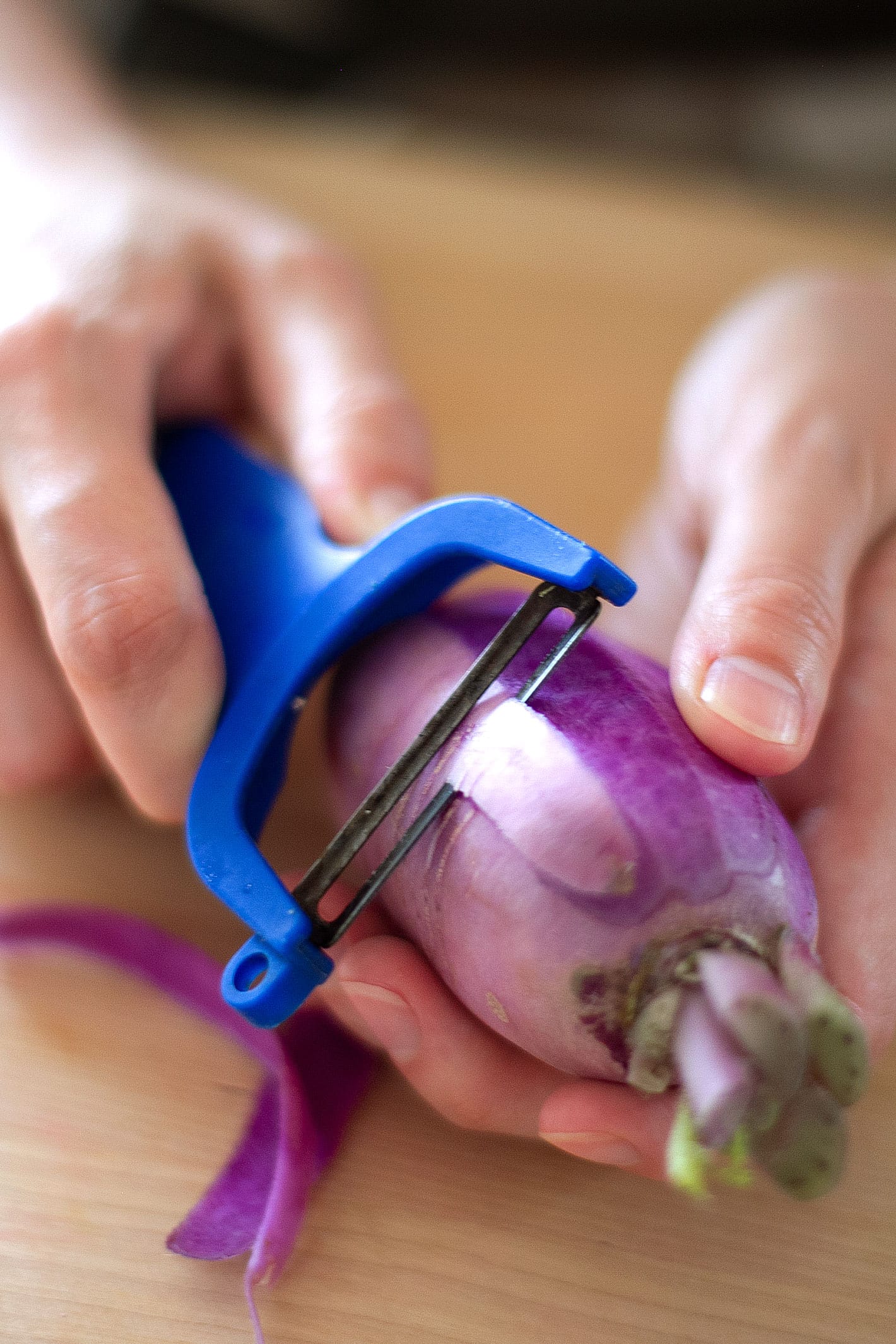 Hands holding a purple daikon radish and peeling it with a vegetable peeler.
