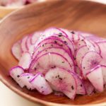 Thinly sliced purple daikon radish dressed with sesame oil, minced garlic, and toasted sesame seeds on a wood plate