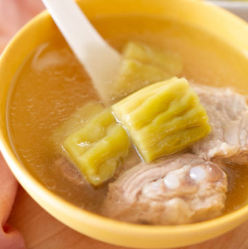 Cooked bitter melon soup with pork ribs in a yellow bowl with a Chinese soup spoon.