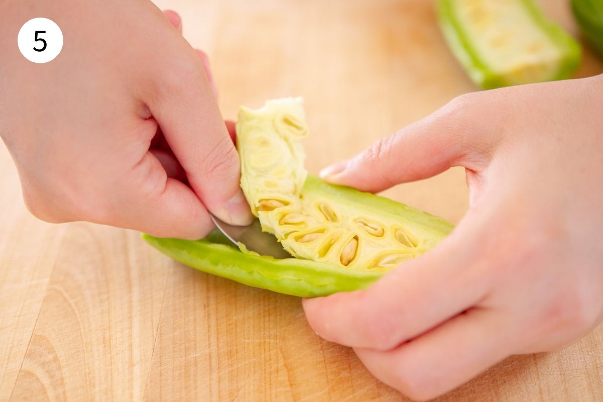 5. Hands using a metal spoon to scoop up seed from a piece of bitter melon.