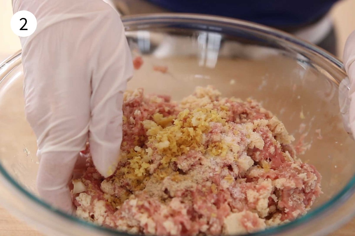 A glove-covered hand mixing turkey and tofu meatball ingredients in a glass bowl.