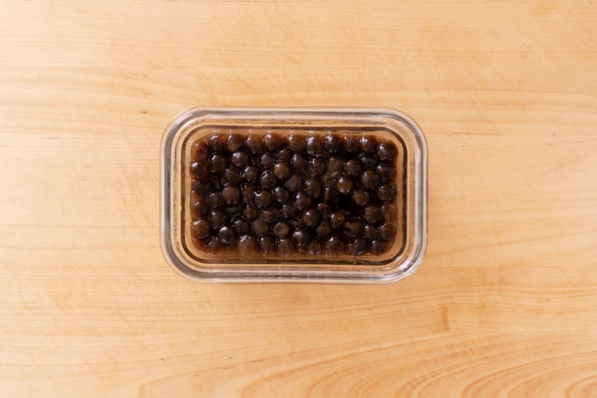 Cooked boba (tapioca pearls) in a small, rectangle glass container on a wood cutting board.