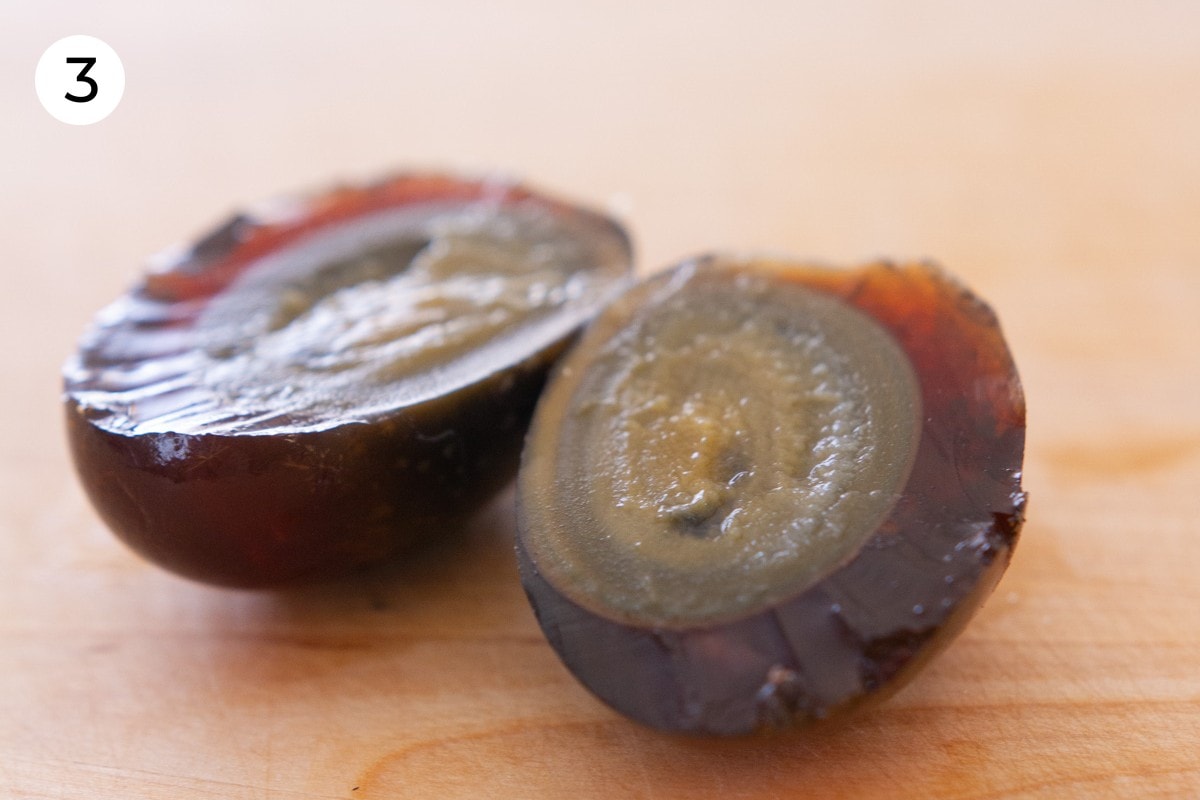 Two halves of a peeled century egg on a wood cutting board.