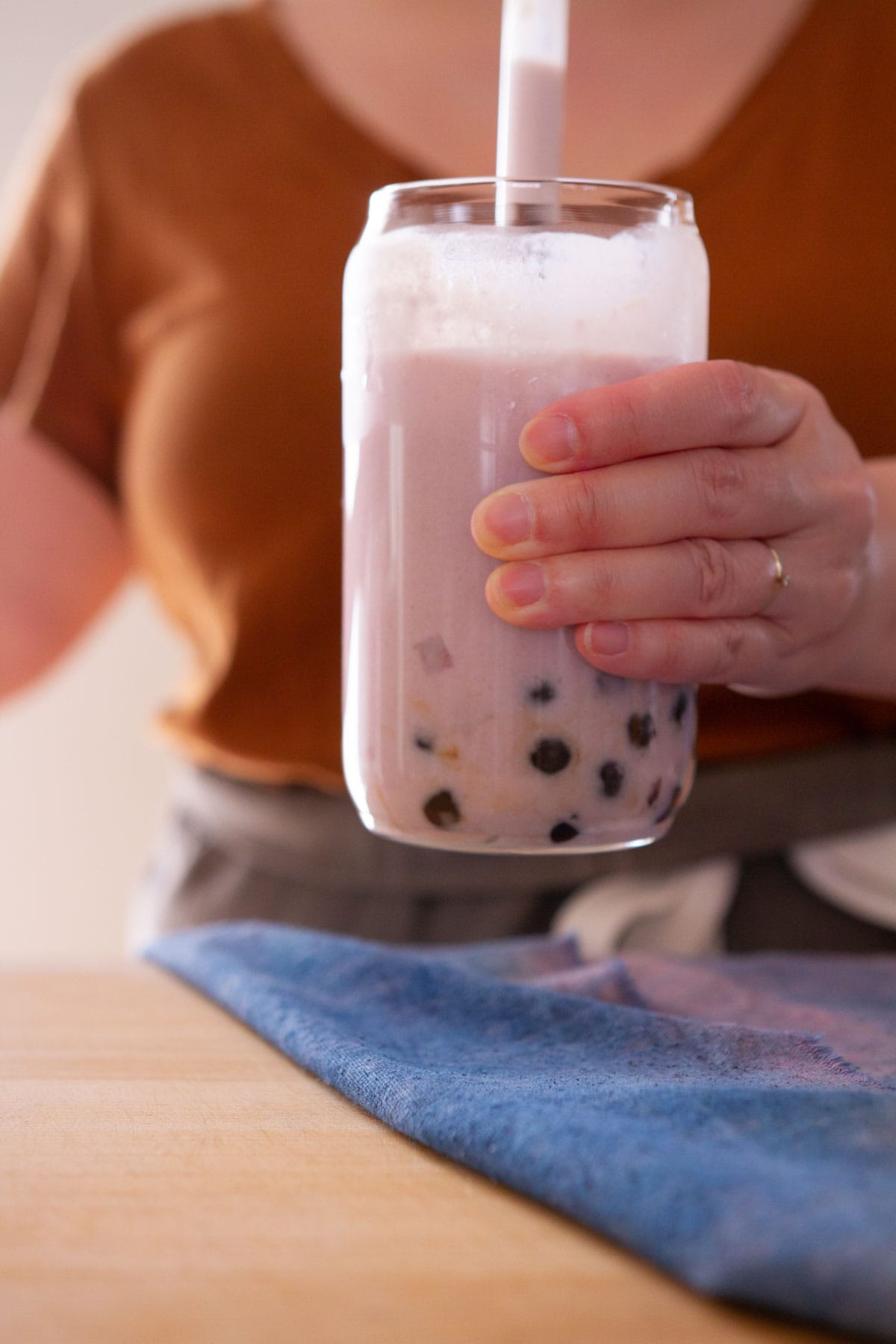 A person picking up a glass of taro boba with a glass straw.