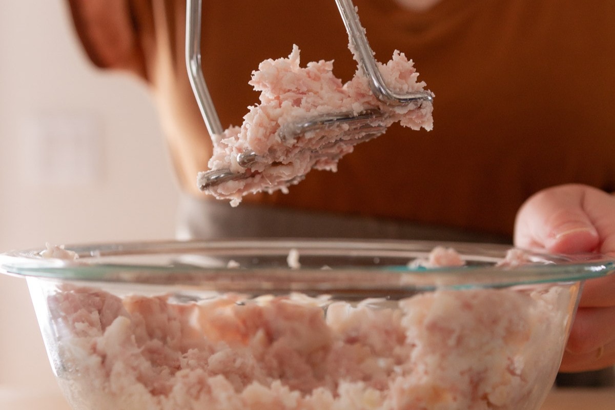 Steamed taro being mashed in a glass mixing bowl with a potato masher.