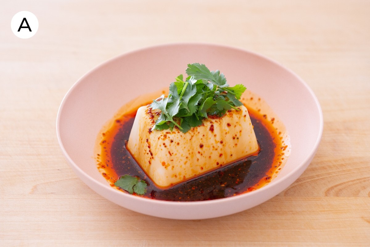 A photo labeled with "A" of silken tofu in a shallow pink bowl, topped with mala chili crisp, soy sauce, sesame oil, and fresh cilantro.