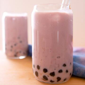 Two taro boba milks in tall glasses on a wood table.