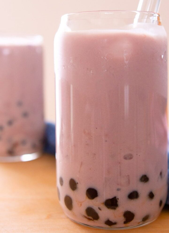 Two taro boba milks in tall glasses on a wood table.