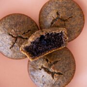 Top down view of stacked black sesame mochi muffins in a pink serving plate, with one cut in half to show the golden crust on the outside and moist black sesame center.