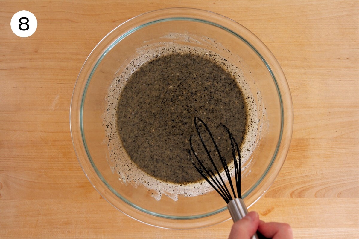 Cindy whisking the black sesame powder into the wet batter until well incorporated in a large mixing bowl, labeled with a circled number "8."