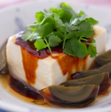 Silken tofu and century egg wedges in a white dish, topped with soy paste, sesame oil, and fresh cilantro.