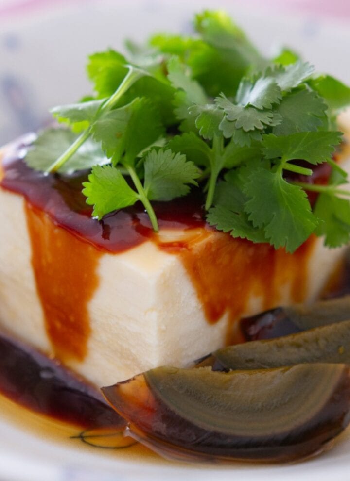 Silken tofu and century egg wedges in a white dish, topped with soy paste, sesame oil, and fresh cilantro.