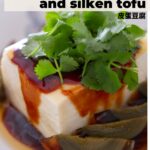 Silken tofu and century egg wedges in a white dish, topped with soy paste, sesame oil, and fresh cilantro with text overlay that says, "simple, umami rich century egg and silken tofu 皮蛋豆腐" and "the sound of cooking dot com" on the bottom next to an illustrated watermelon logo.