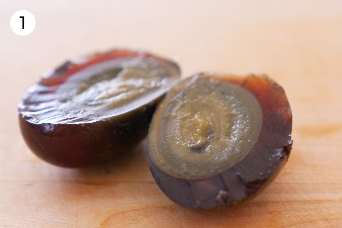 A century egg cut in half on a wood cutting board, labeled with a circled number "1."