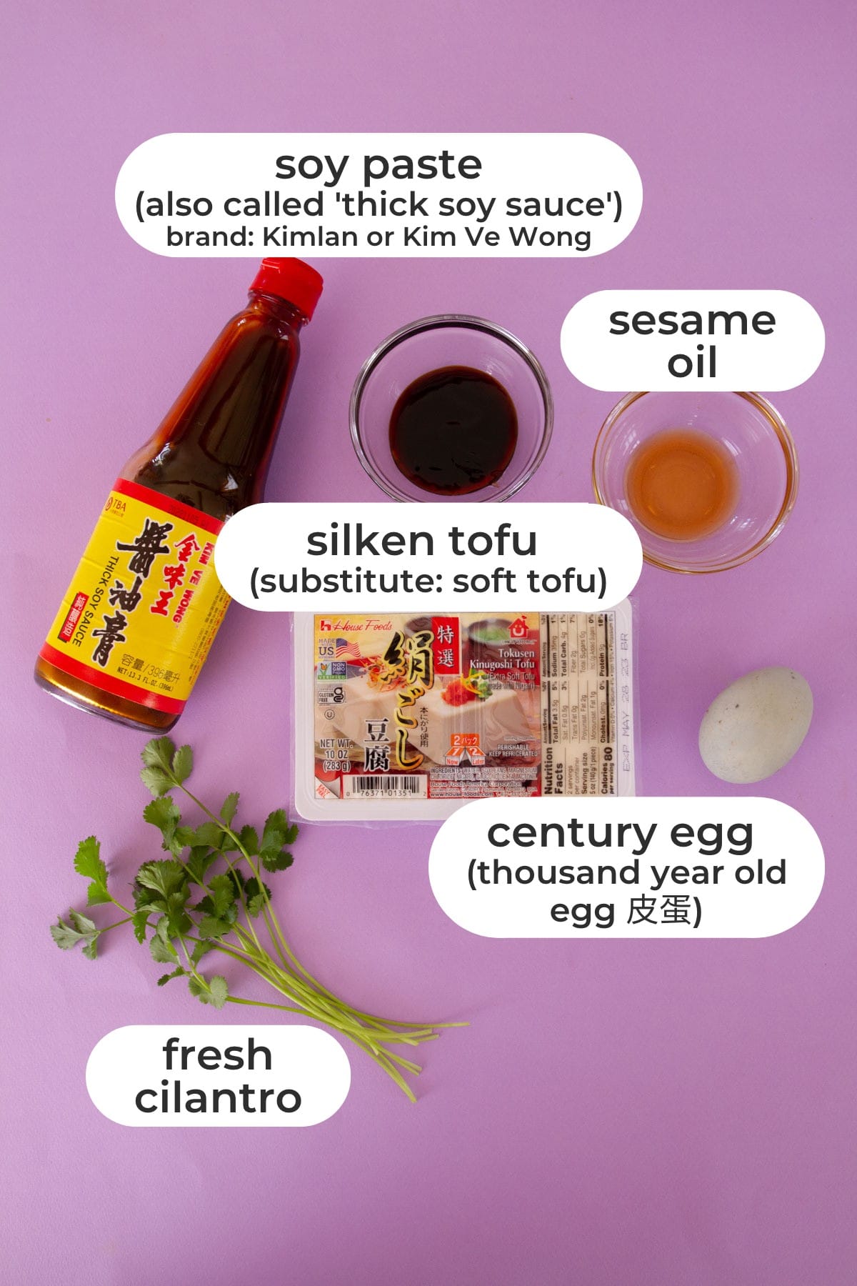 Ingredients for this recipe laid out on top of a purple background and labeled as: "soy paste (also called 'thick soy sauce', brand: Kimlan or Kim Ve Wong)," "sesame oil," "silken tofu (substitute: soft tofu)," "century egg (thousand year old egg 皮蛋," and "fresh cilantro."