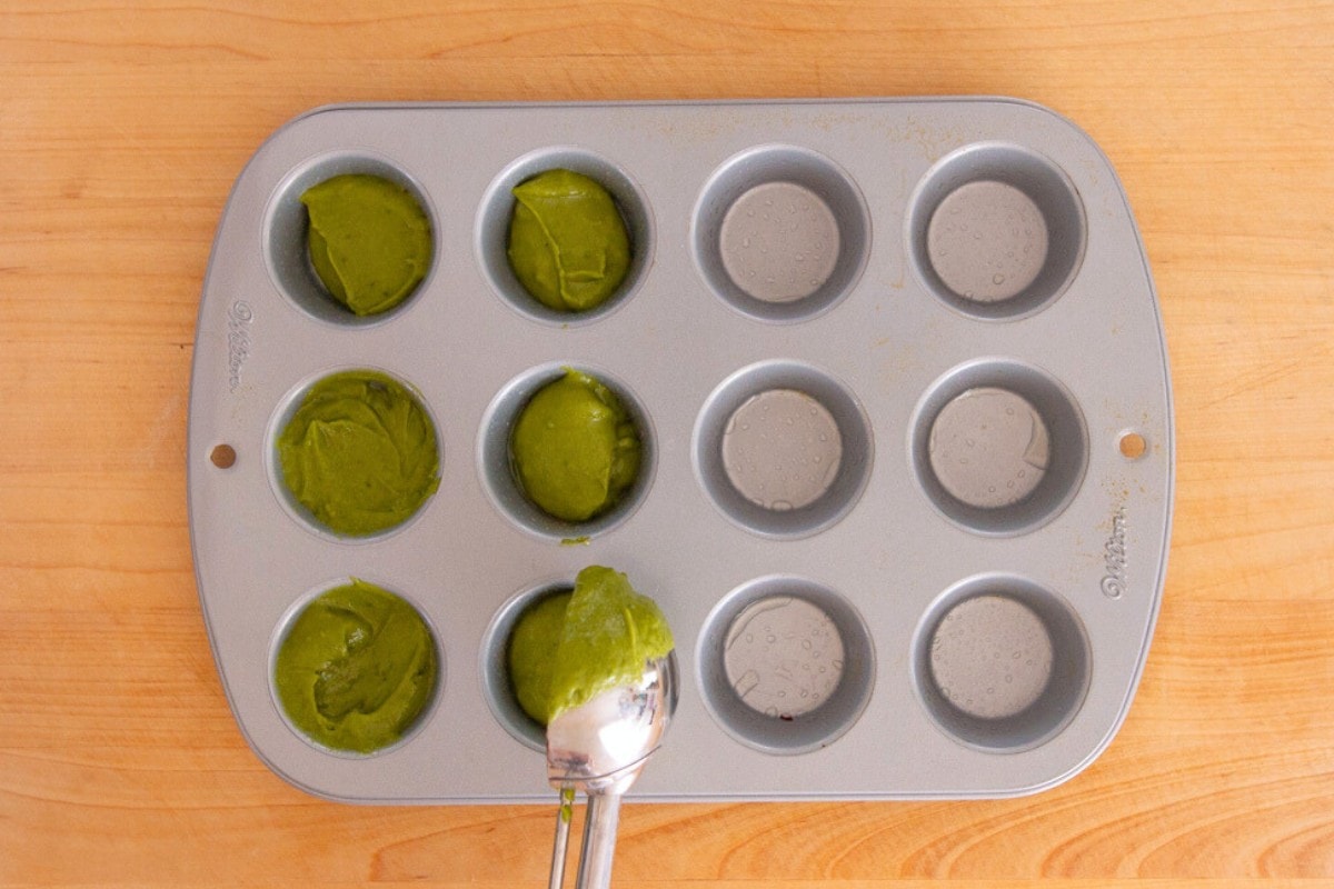 Cindy using a cookie scoop to equally divide the macha mochi muffin batter in a mini muffin pan.