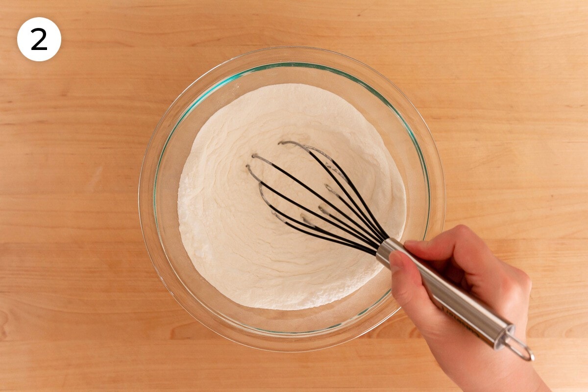 Cindy mixing dry ingredients in a medium glass mixing bowl with a whisk, labeled with a circled number "2."