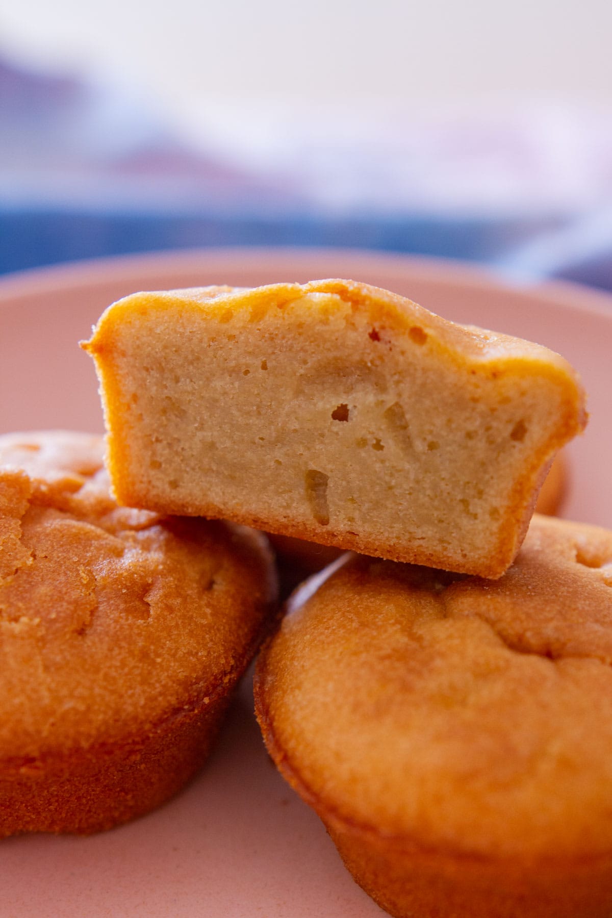 Close up view of stacked mochi muffins in a pink serving plate, with the top one cut in half to show the golden crust on the outside and moist center.