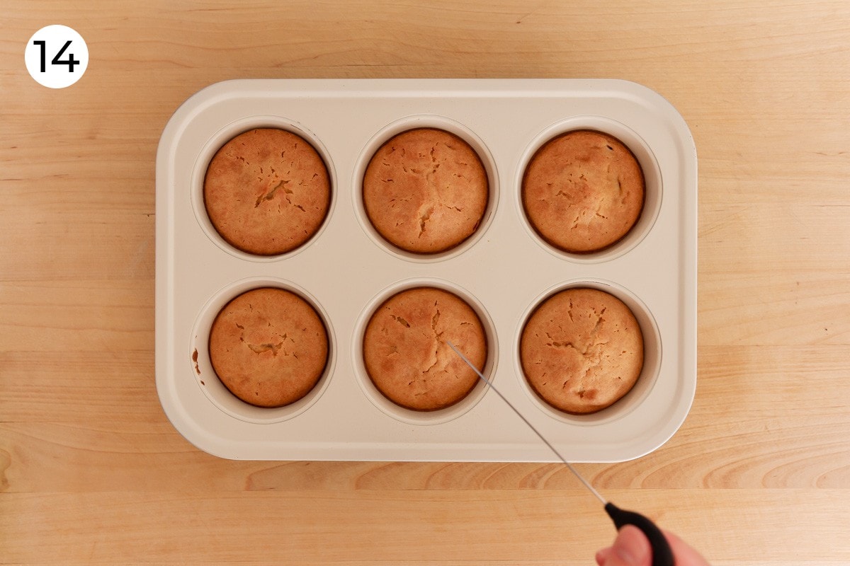 Cindy holding a cake tester with a clean tip above a pan of baked mochi muffins, labeled with a circled number "14."