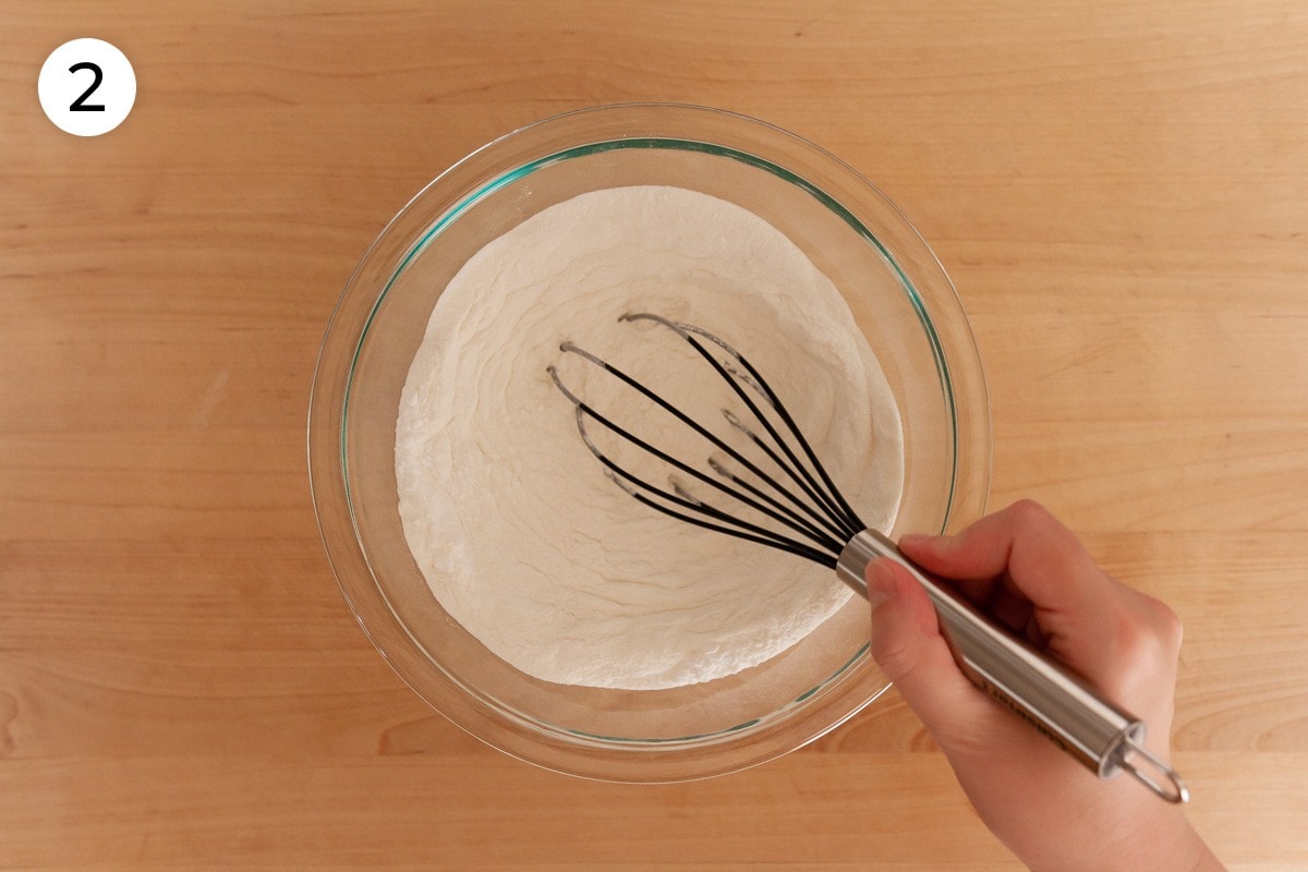 Cindy mixing dry ingredients in a medium glass mixing bowl with a whisk, labeled with a circled number "2."