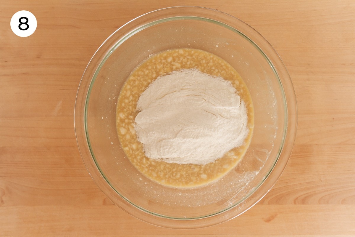 Mixed dry ingredients added to the top of the wet batter in the large glass bowl, labeled with a circled number "8."