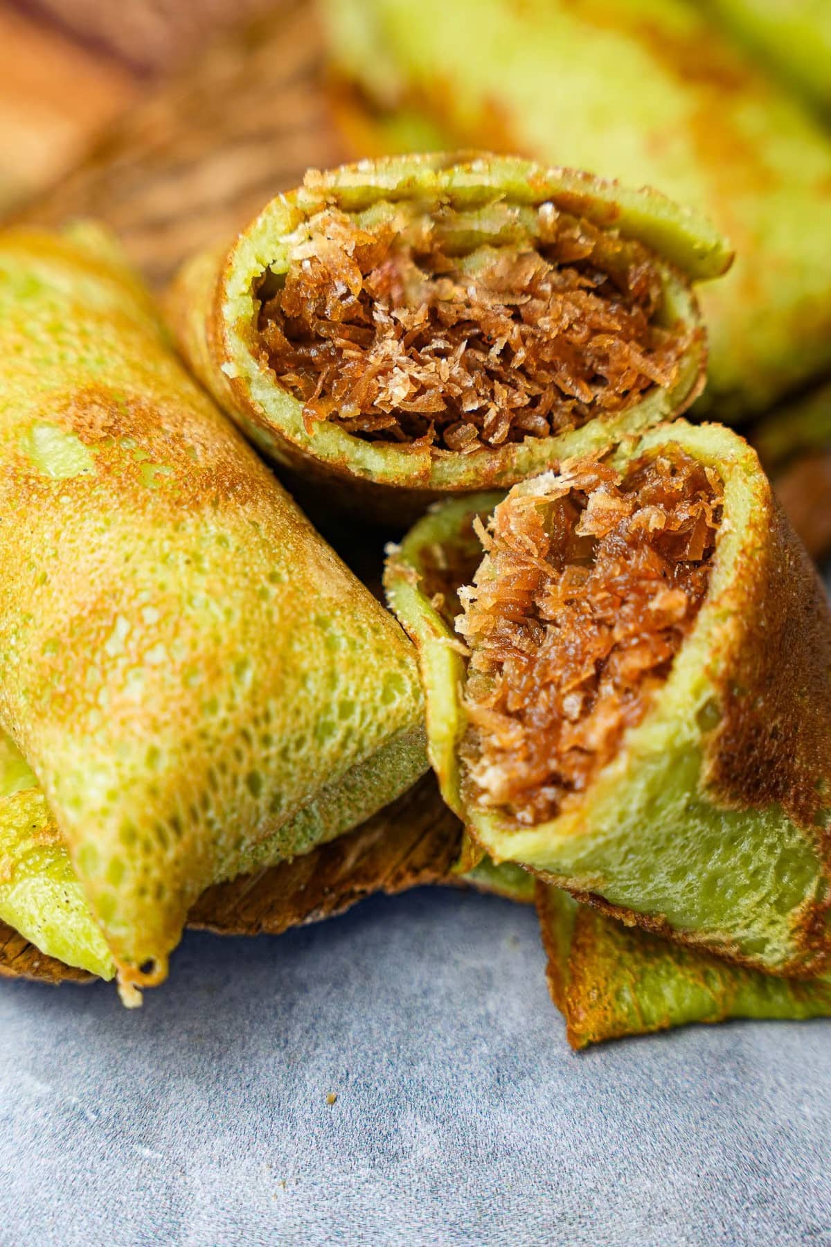 Four wrapped portions of kuih dadar on a wooden board, with one cut open to show the coconut filling inside.