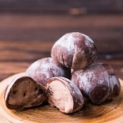 Chocolate mochi ice cream stacked on a plate with a few cut open to show the filling.