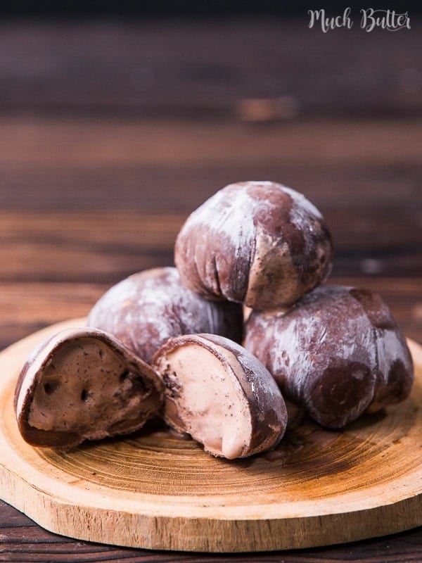 Chocolate mochi ice cream stacked on a plate with a few cut open to show the filling.