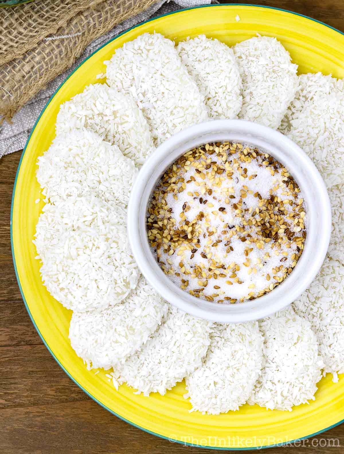 Palitaw fanned out on a yellow plate with toasted sesame and sugar topping in the middle.
