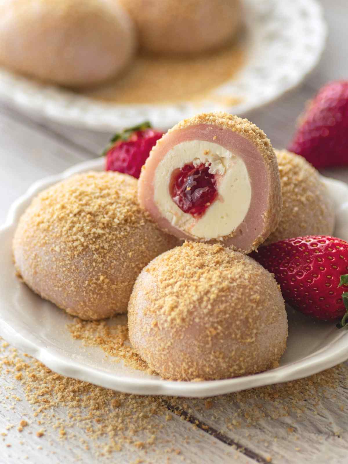 Three strawberry cheesecake mochi on a white plate with mochi cut in half on top.