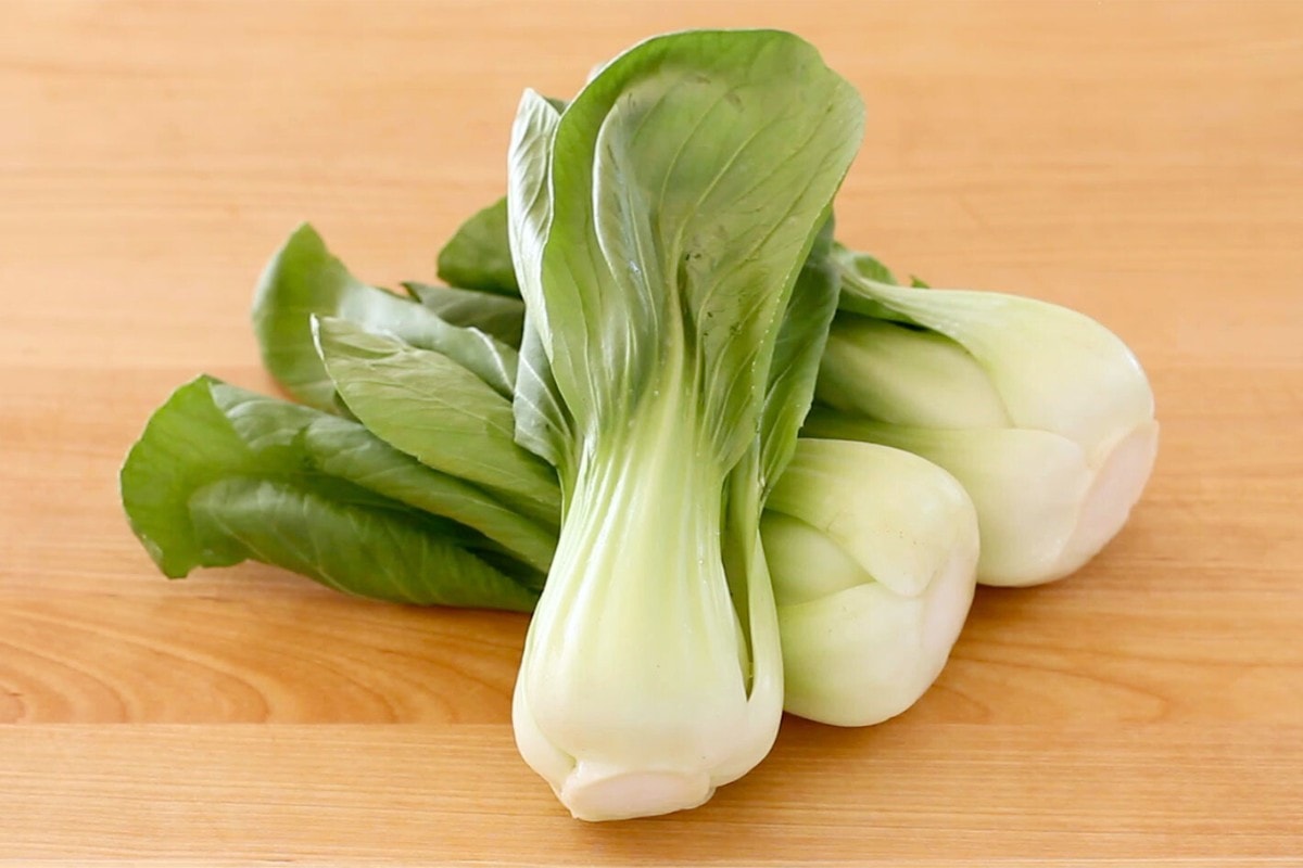 Three Shanghai baby bok choys on a wood cutting board.