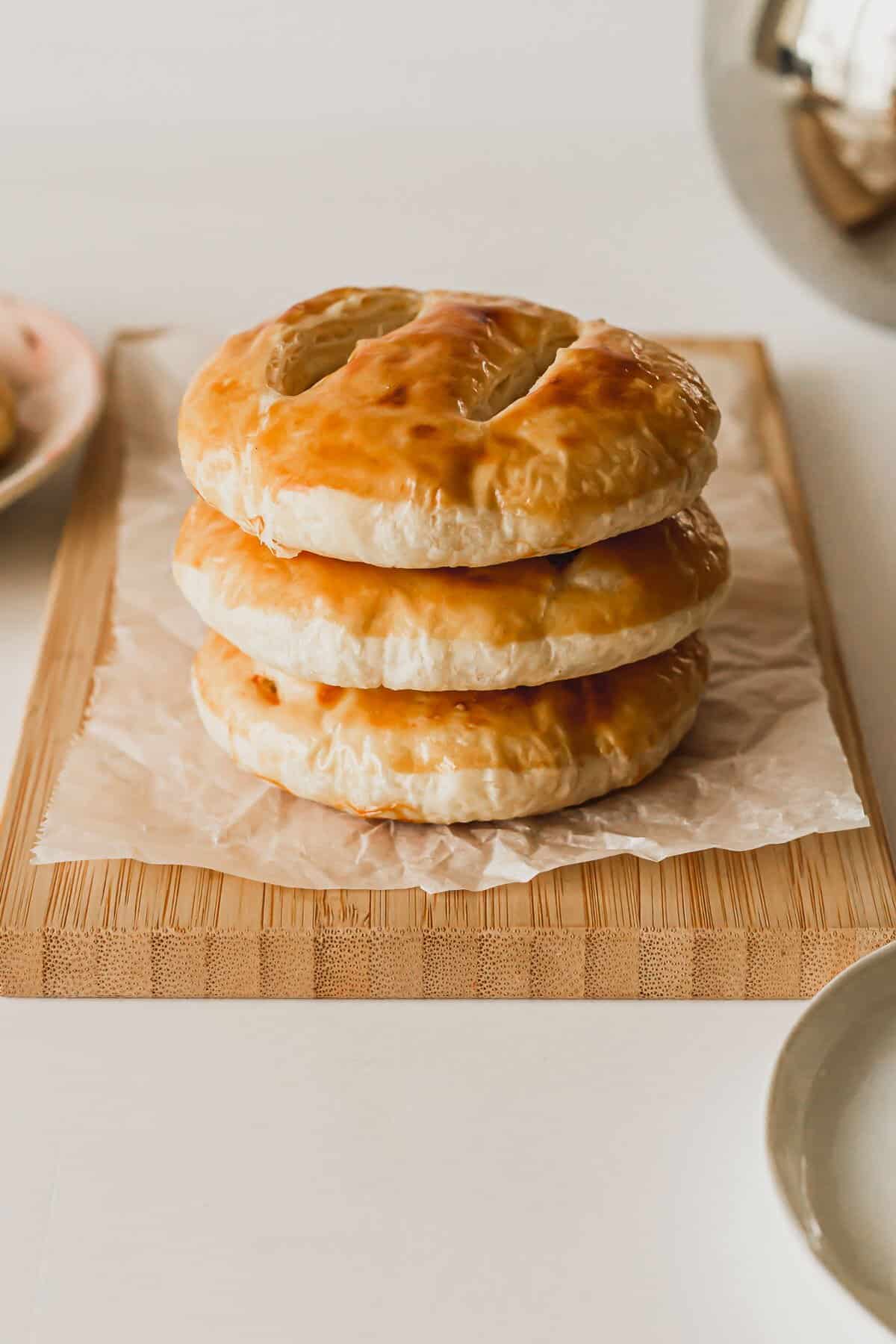 Three Chinese wife cakes stacked on a parchment covered bamboo cutting board.